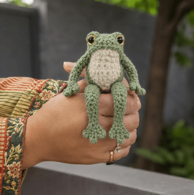 Small sage green crochet frog held in a person's hand