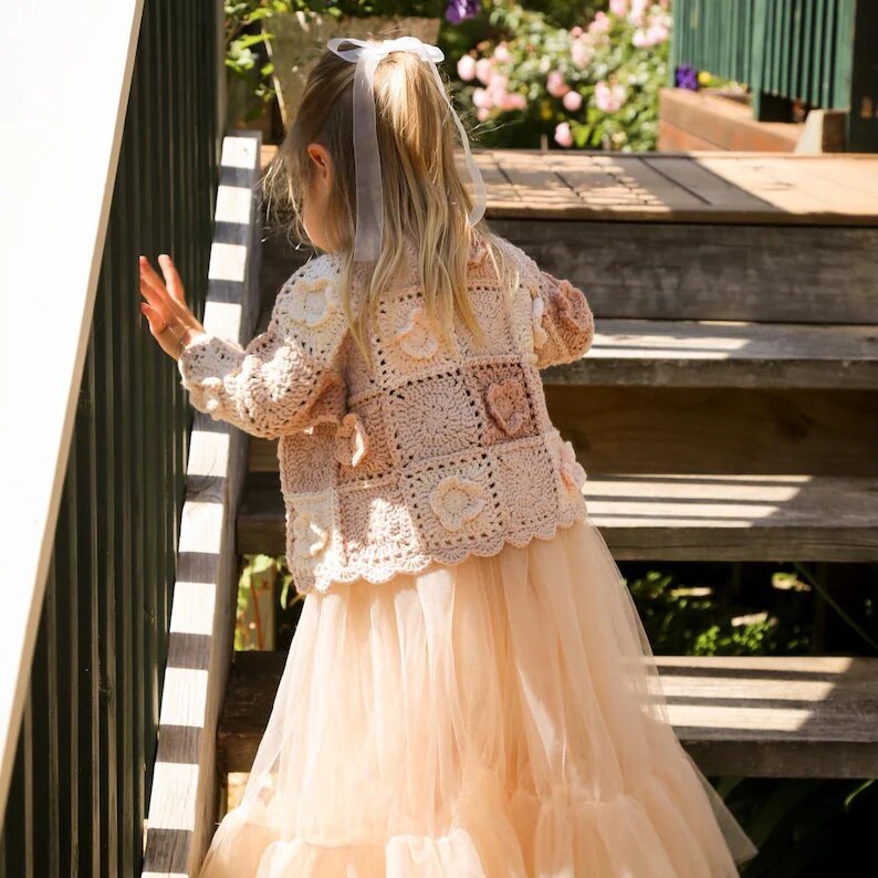 Children outdoors wearing pink, cream and taupe flower granny square cardigans.