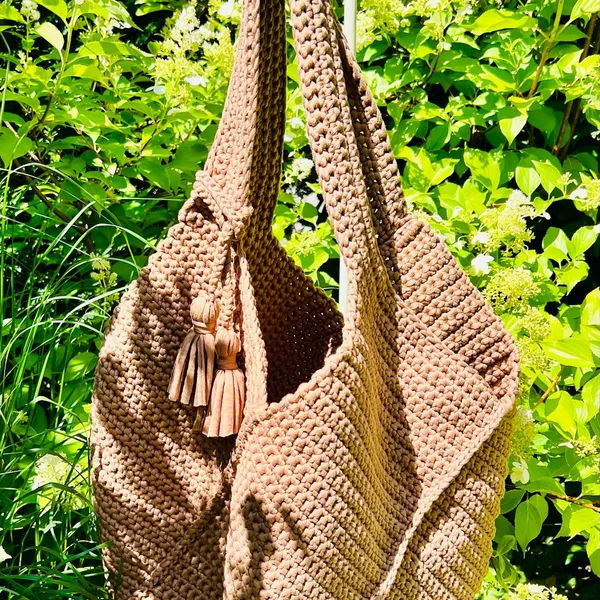 Brown handmade crochet shoulder bag with long straps and tassel details outdoors.