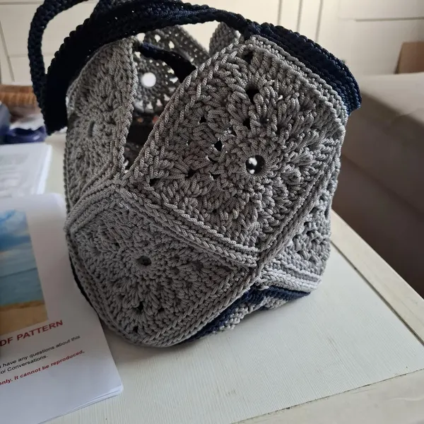 Charcoal gray granny square crochet bag with dark handles on a white table.