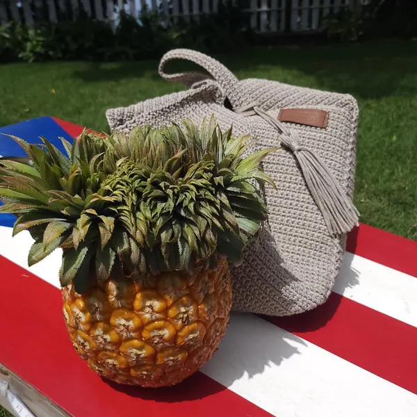 Structured gray crochet handbag with a tassel photographed outdoors.