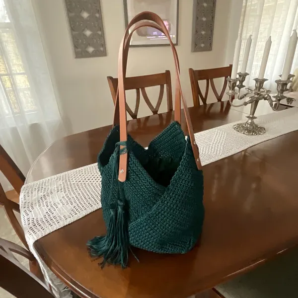 Dark green crochet tote bag with tan leather handles and tassels.